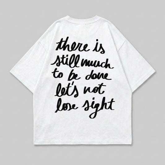 White t-shirt with black handwritten text "there is still much to be done let's not lose sight".