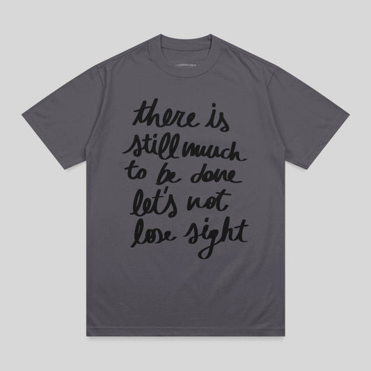 Dark grey t-shirt with "there is still much to be done let's not lose sight" in black script.