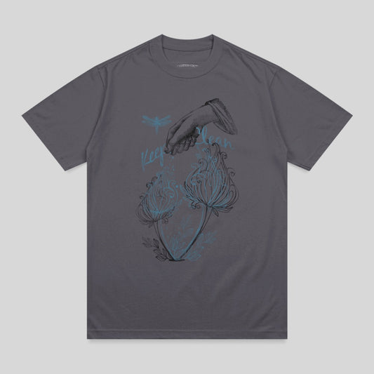 Dark grey t-shirt with illustration of hand, dragonflies, and glowing flowers.