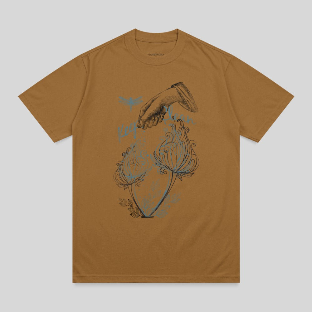 Brown t-shirt with a line drawing of a hand pouring water over two flowers.