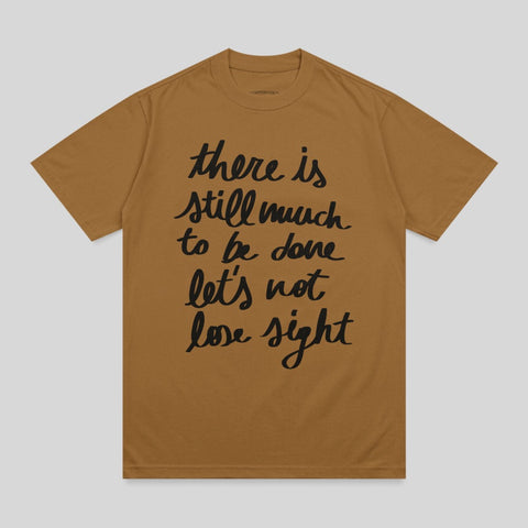 Brown t-shirt with black text "there is still much to be done let's not lose sight".
