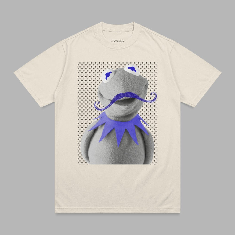 Kermit the Frog with a purple mustache and blue eyes on a cream t-shirt.