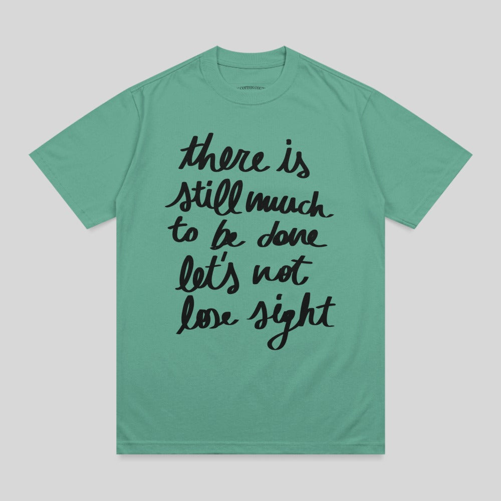 Green t-shirt with black text "there is still much to be done let's not lose sight".