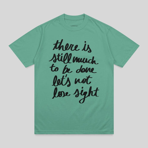 Green t-shirt with black text "there is still much to be done let's not lose sight".