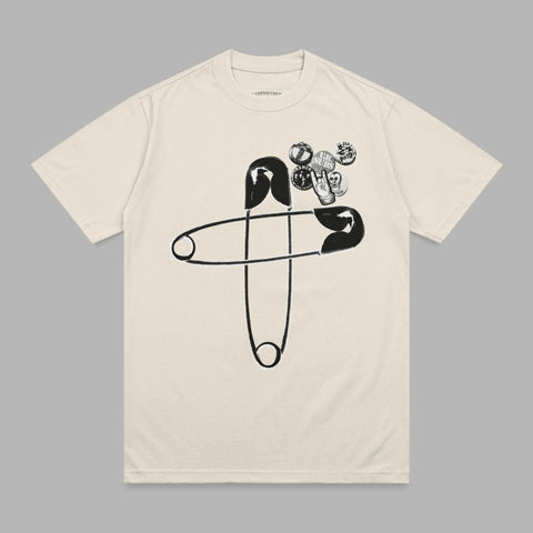 Cream t-shirt with black safety pin and collection of graphic pins.