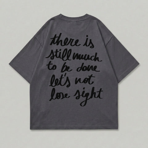 Dark grey t-shirt with black text: "there is still much to be done let's not lose sight".