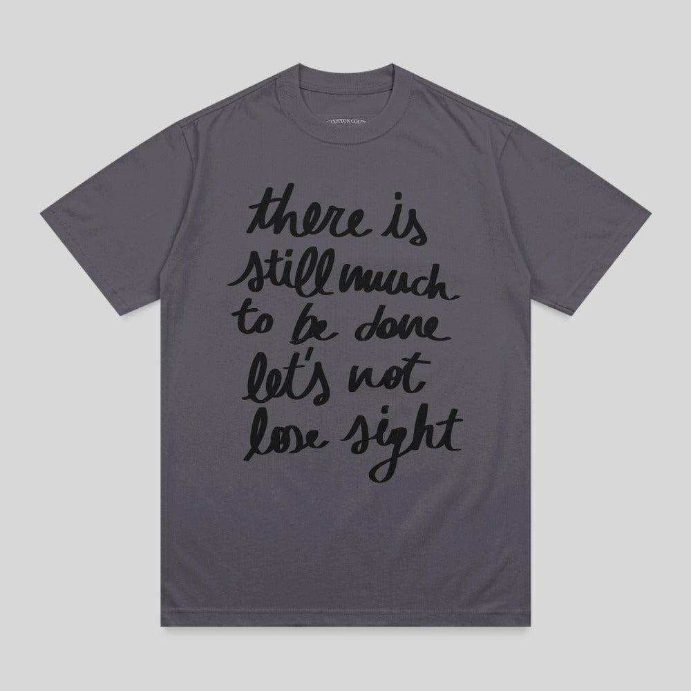 Dark grey t-shirt with "there is still much to be done let's not lose sight" in black script.