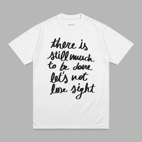 White t-shirt with black script text "there is still much to be done let's not lose sight".