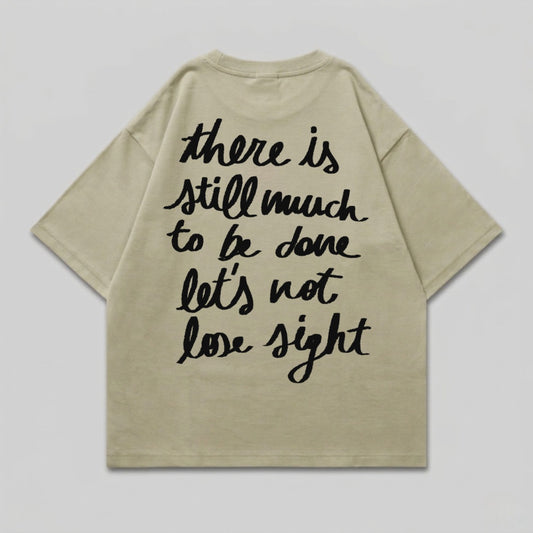 Light tan t-shirt with black script text: "there is still much to be done let's not lose sight".