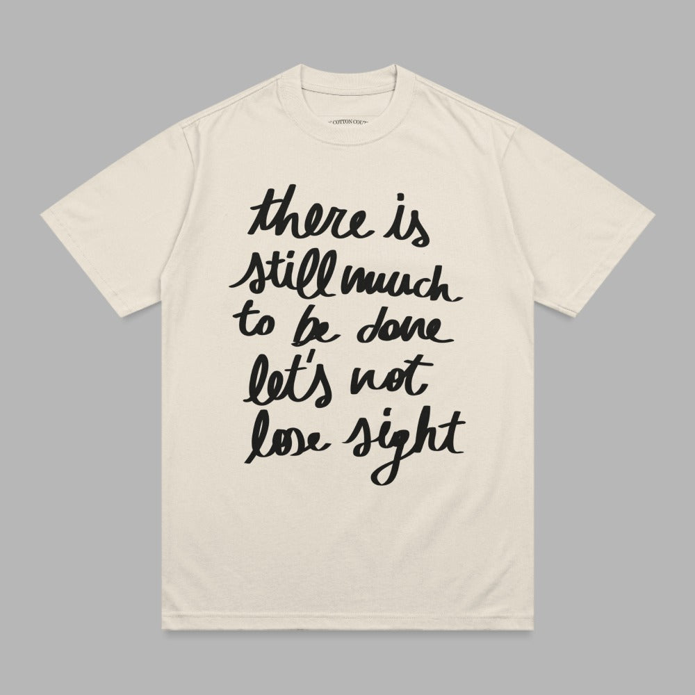 Cream t-shirt with black handwritten text "there is still much to be done let's not lose sight".