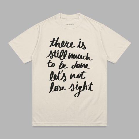 Cream t-shirt with black handwritten text "there is still much to be done let's not lose sight".
